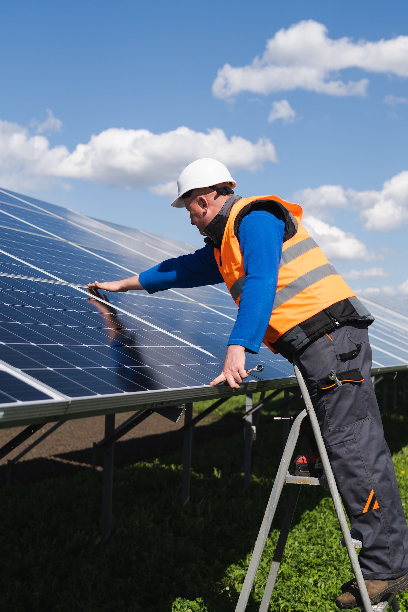 Solar power plant worker on stepladder makes a visual inspection of solar panels